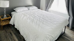 A bedroom with a bed, a bedside table with a lamp, grey curtains, and a window.