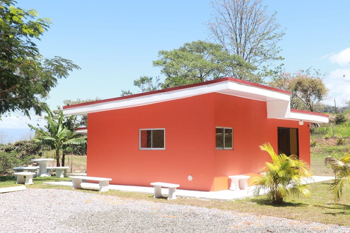 Un bâtiment rouge avec un toit blanc, entouré d’une zone recouverte de gravier et de plusieurs bancs blancs.