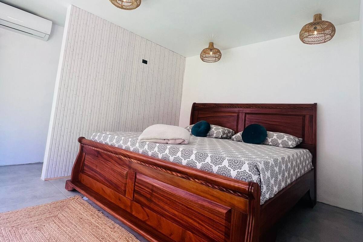 Une chambre à coucher avec un lit en bois, une tête de lit en osier, un mur blanc et un ventilateur de plafond.