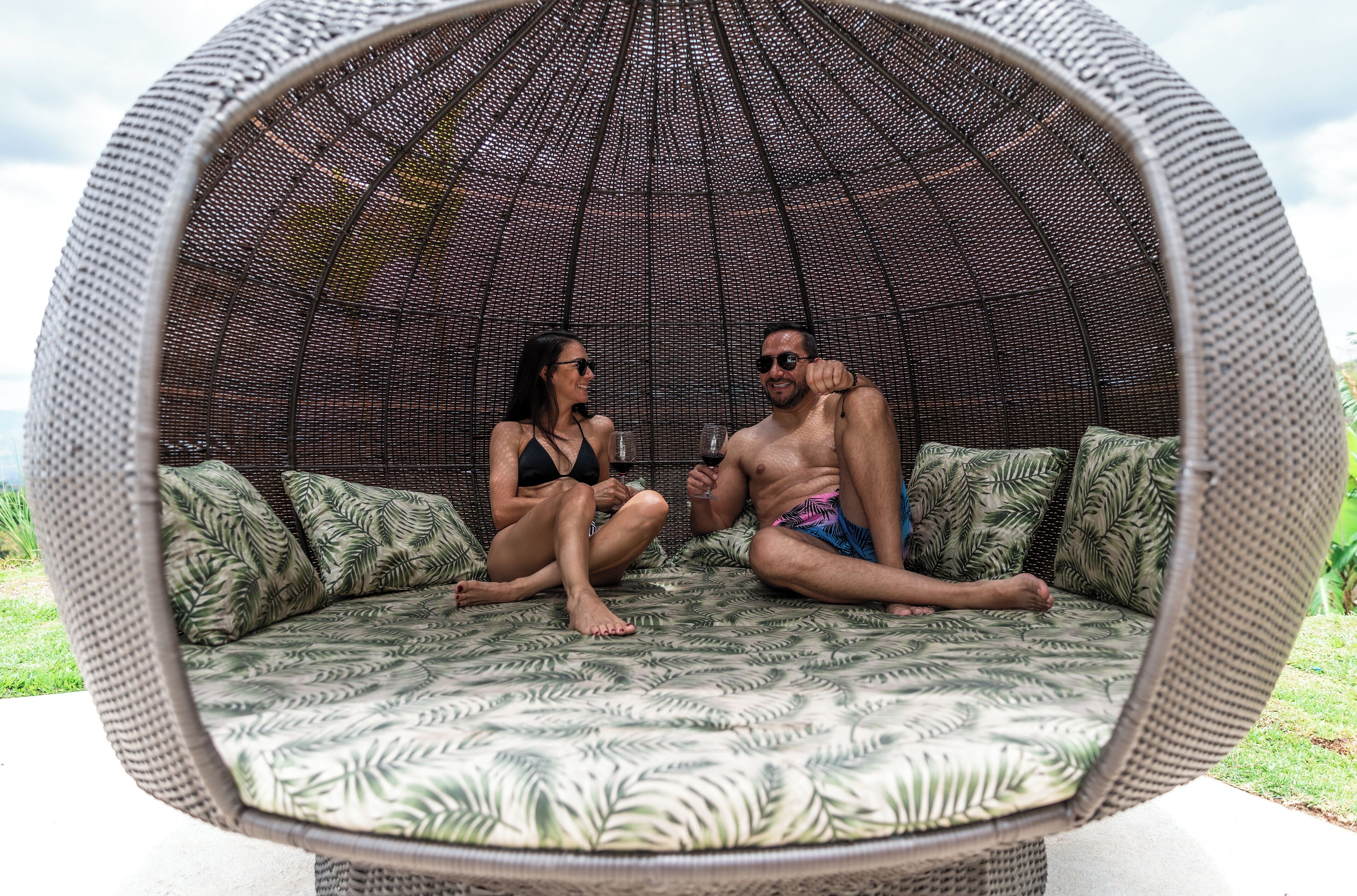 A wicker outdoor seating area with a patterned cushion, a mesh roof, and a view of the outdoors.