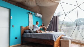 A bedroom with a wooden bed, a teal wall, and a view through a geometric window structure.