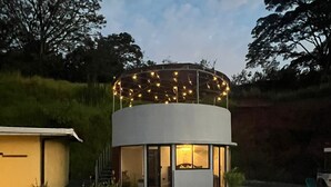 A modern house with a circular design, a pool, and string lights on the roof.