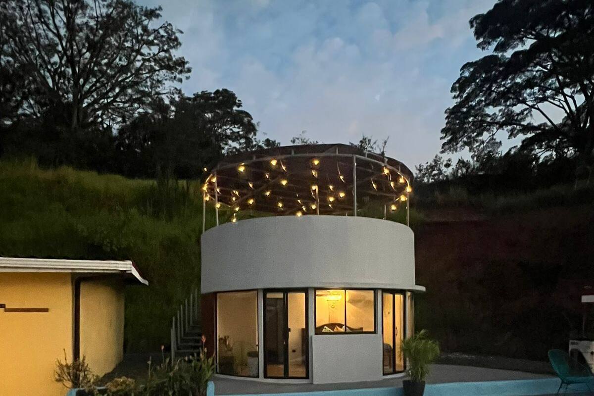 Une maison moderne à la conception circulaire, dotée d’une piscine et illuminée de guirlandes lumineuses sur le toit.