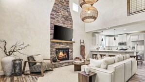 A spacious living room with a stone fireplace, a white sofa, and a kitchen area in the background.