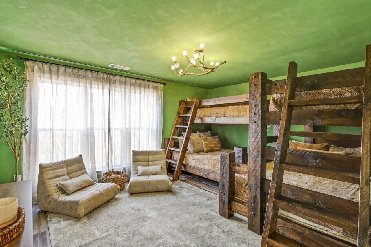 Ein Zimmer mit Etagenbetten, einer Stehleiter, einer gepolsterten Bank und einem Kronleuchter.
