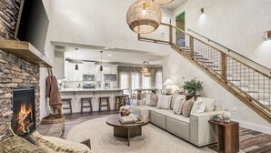 A spacious living area with a stone fireplace, a large sofa, a coffee table, and a staircase leading to an upper level.