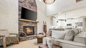 A modern living room with a stone fireplace, a sofa, a coffee table, and a kitchen in the background.
