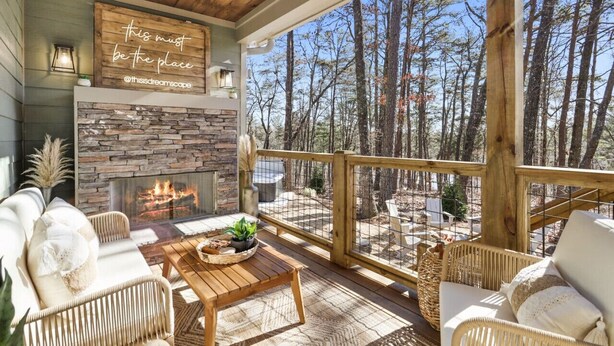 A cozy outdoor seating area with wicker furniture, a stone fireplace, and a view of a forest.