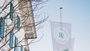 A building with a sign that reads "Klostermaier" and a banner with a logo and text. - Klostermaier Hotel & Restaurant (Icking)