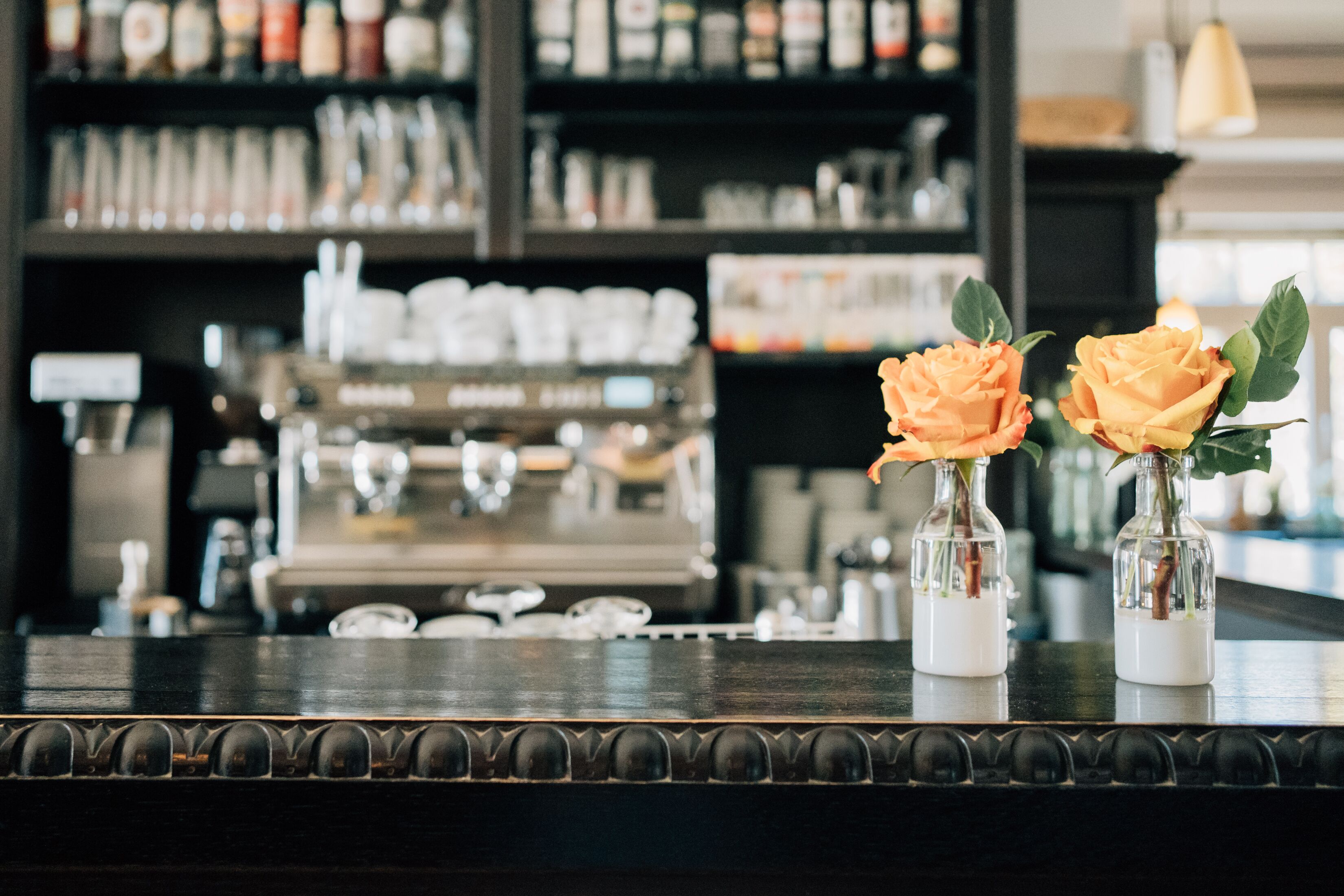 Un comptoir de bar orné de deux vases en verre contenant des roses oranges.