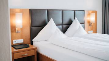 Cama bem arrumada com lençóis brancos e cabeceira escura. Há duas mesas de cabeceira, cada uma com uma luminária e uma tomada.