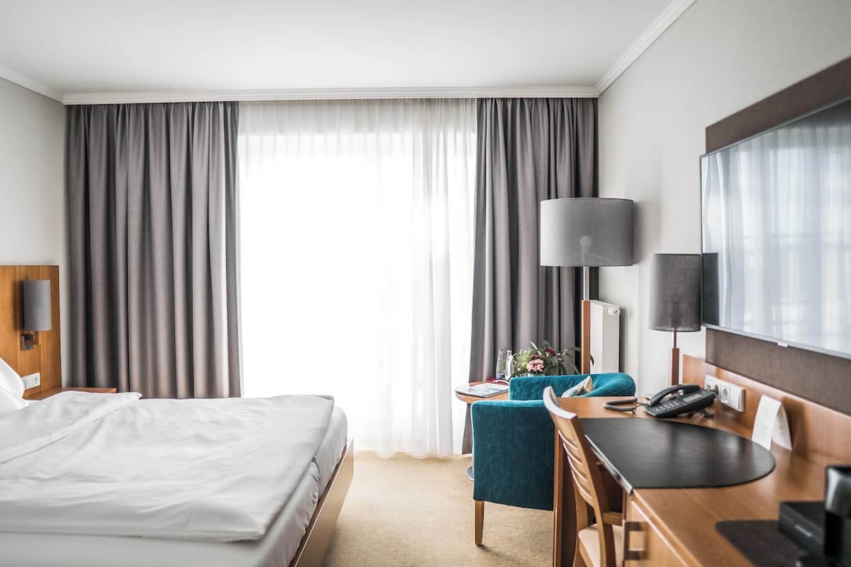A hotel room with a bed, desk, chair, lamp, and TV.