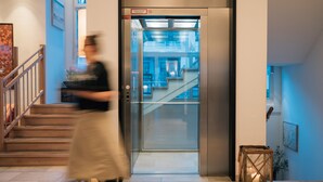 An elevator with a glass door, a staircase with wooden steps, and a small table with a candle. - Klostermaier Hotel & Restaurant (Icking)