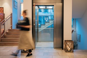 An elevator with a glass door, a staircase with wooden steps, and a small table with a candle.