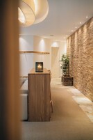 A modern interior with a wooden reception desk, a stone wall, and a hanging light fixture.