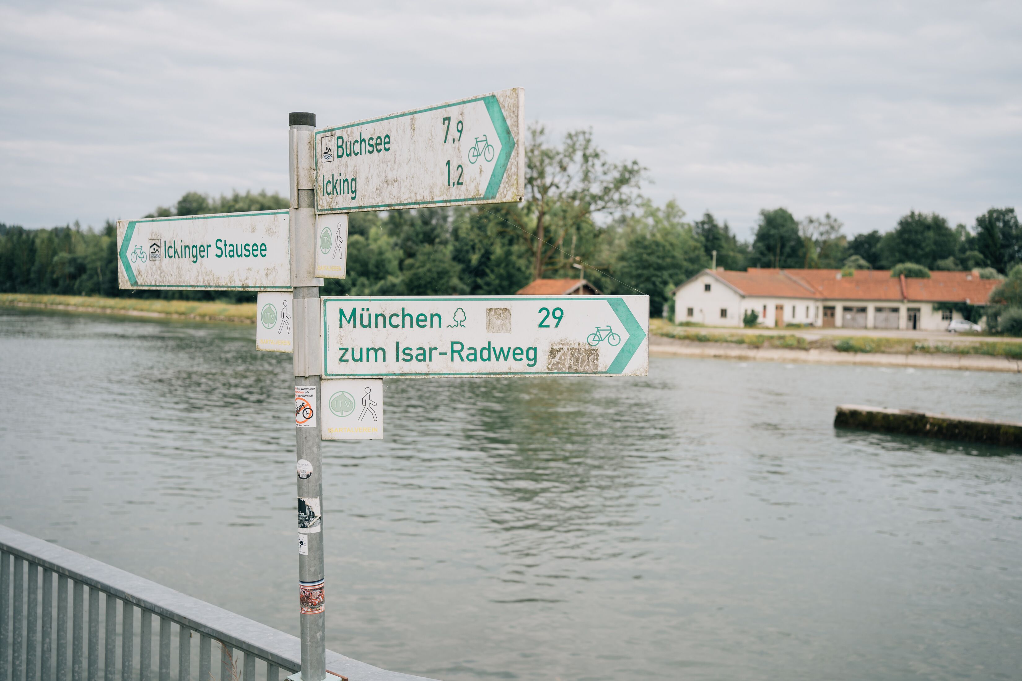 Wegweiser an einem Gewässer, im Hintergrund ein Gebäude.