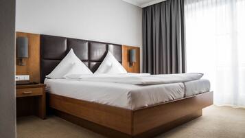 Ein modernes Hotelzimmer mit einem großen Bett, einem Holz-Kopfteil, zwei Nachttischen und Blick ins Freie durch transparente Vorhänge.