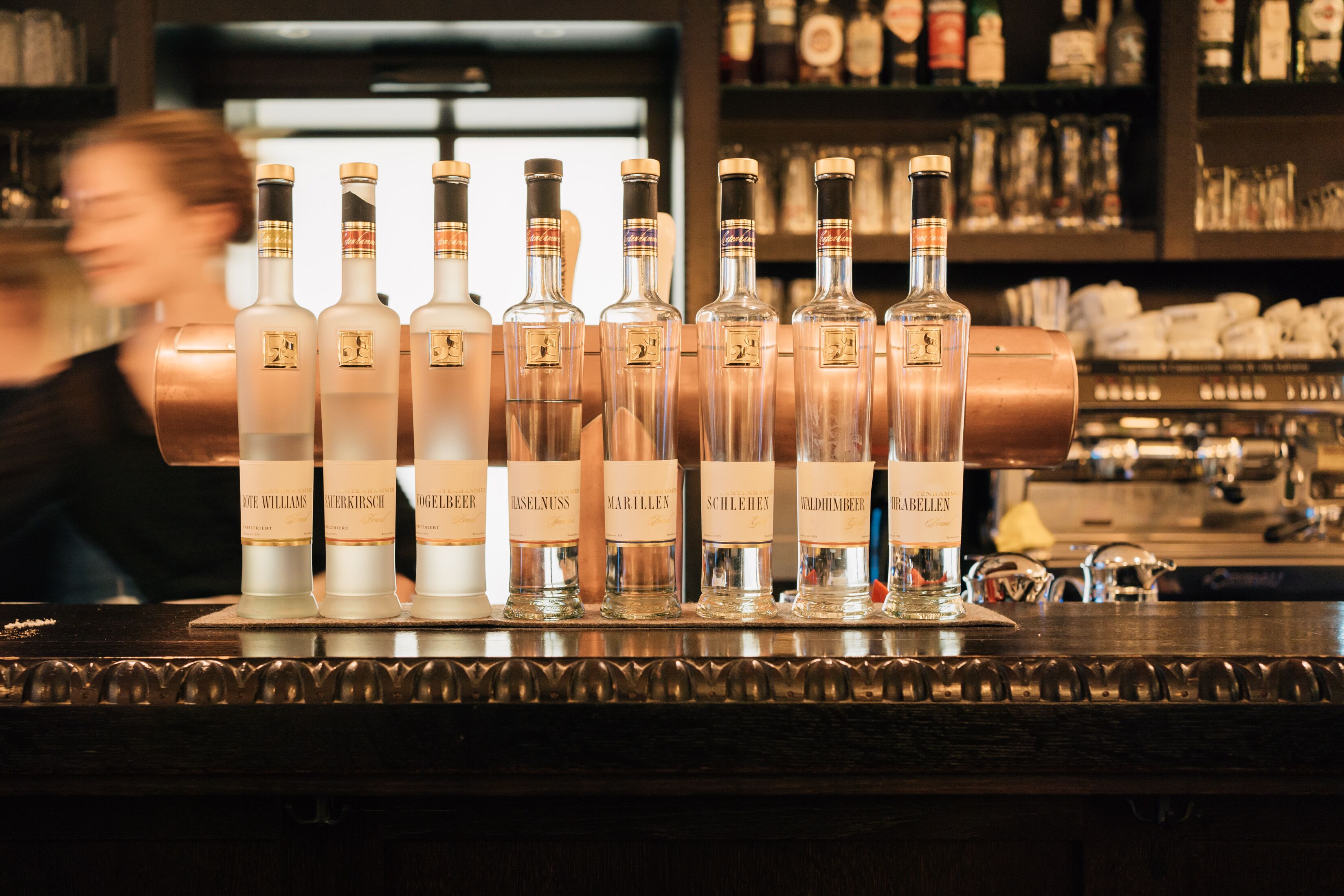 A bar counter with a row of bottles labeled with various names.