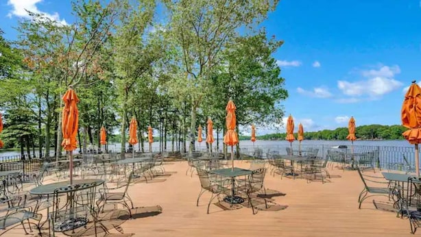 An outdoor patio with tables and chairs, surrounded by orange umbrellas, overlooking a body of water.
