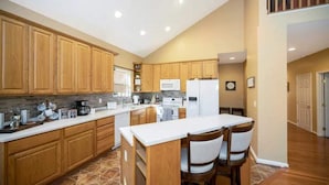 A modern kitchen with wooden cabinets, a white countertop, and a breakfast bar with chairs.