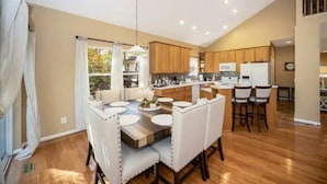 A modern kitchen with wooden cabinets, a central island, and a dining area with white chairs and a wooden table.