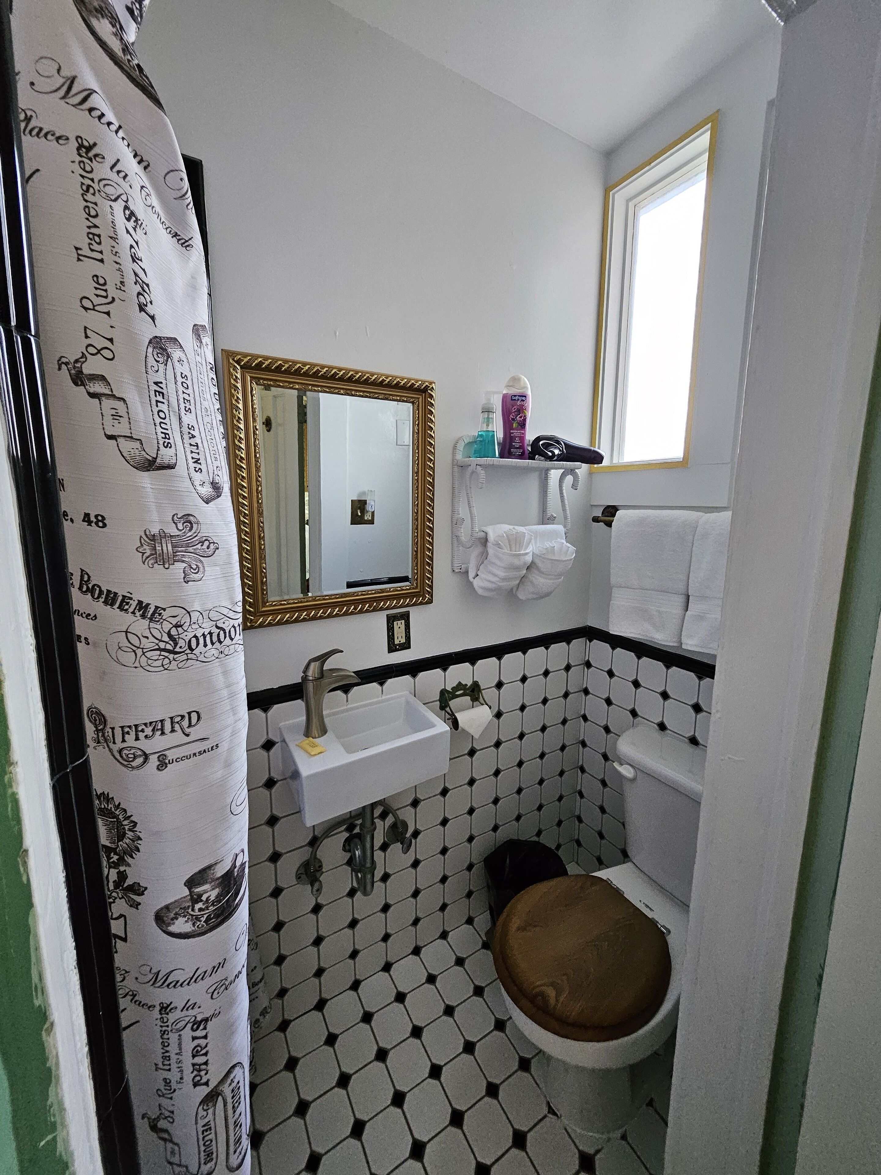 Une salle de bain avec un sol carrelé en noir et blanc, un lavabo blanc avec un robinet doré, des toilettes avec un abattant marron et un miroir avec un cadre doré.