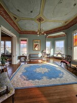 Amplia habitación con alfombra grande de diseño azul y blanco, suelo de madera y techo alto con molduras decorativas.