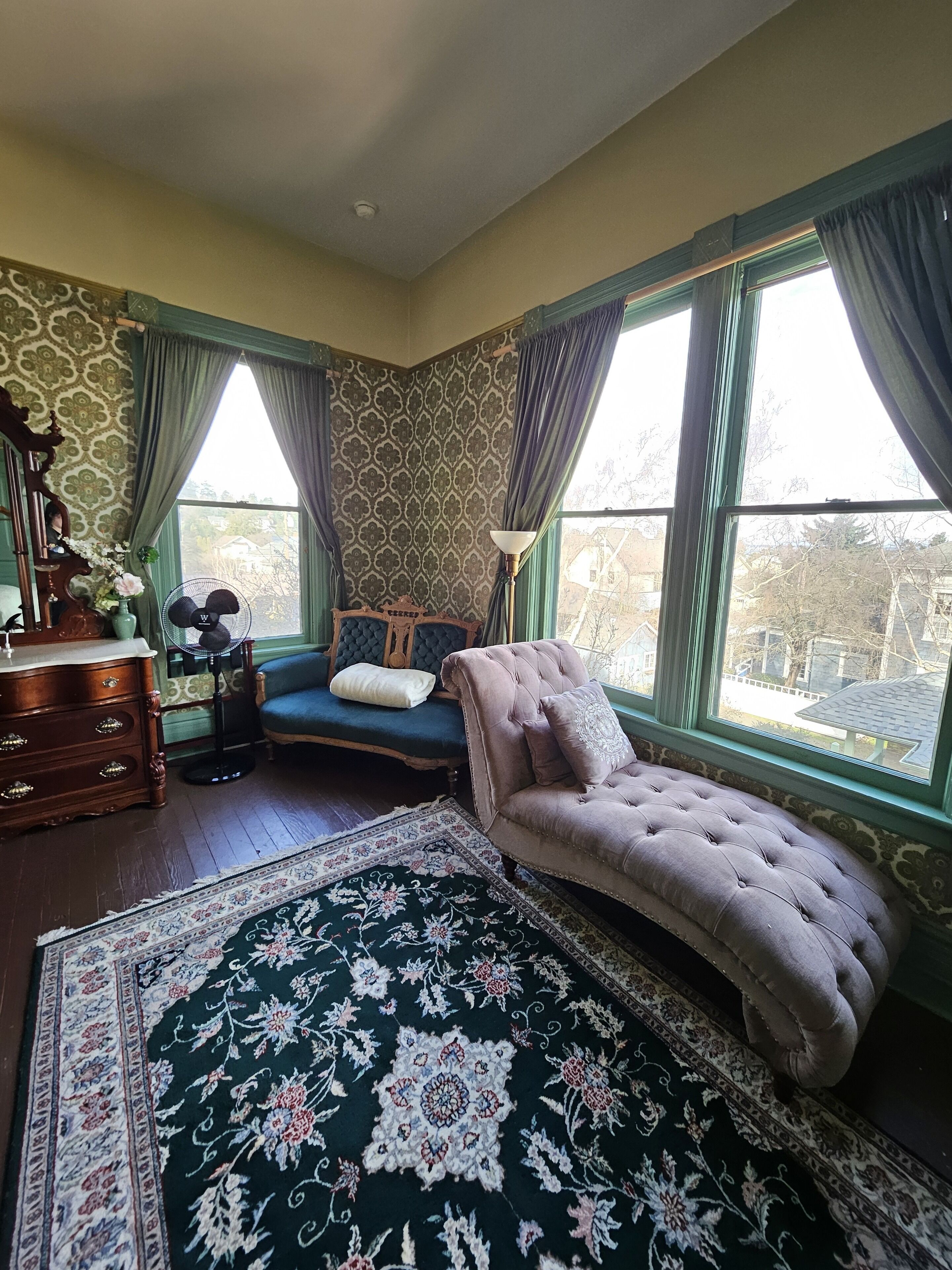 A bedroom with a large bed, a dresser, a chair, and a window with curtains.
