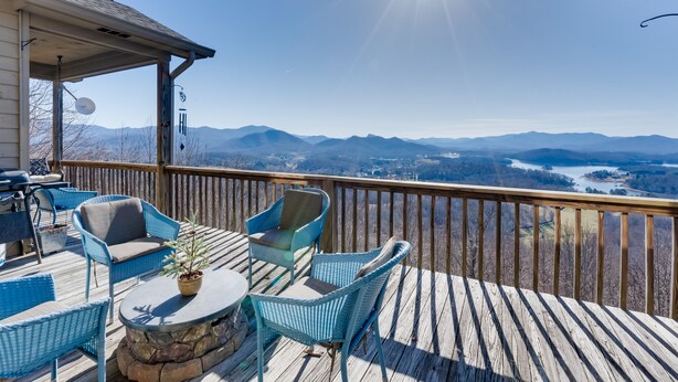 Eine Holzdielen-Terrasse mit Korbmöbeln und einem Blumentopf, mit Blick auf eine Berglandschaft.