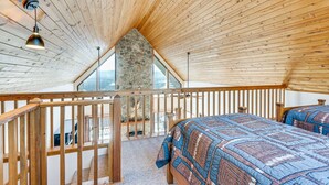 Ein Schlafzimmer mit schrägen Wänden, Holzbalken, einem Steinofen und einem großen Fenster.