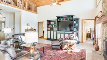 A spacious living room with a high ceiling, a fireplace, a large TV, and a cozy seating area with leather sofas and a patterned rug.