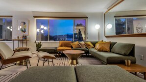 Uma sala de estar moderna com um sofá modular, uma mesa de centro e uma mesa lateral. Há uma janela grande com vista para o exterior.
