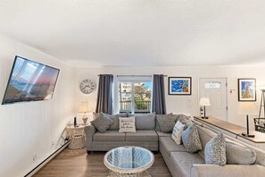 A living room with a sofa, a glass coffee table, a TV, and a window with curtains. - Walk-to-Beach Oceanside Condo (Ocean City)