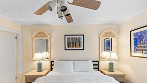 A hotel room with a bed, two nightstands, a ceiling fan, a framed picture, and a poster on the wall.