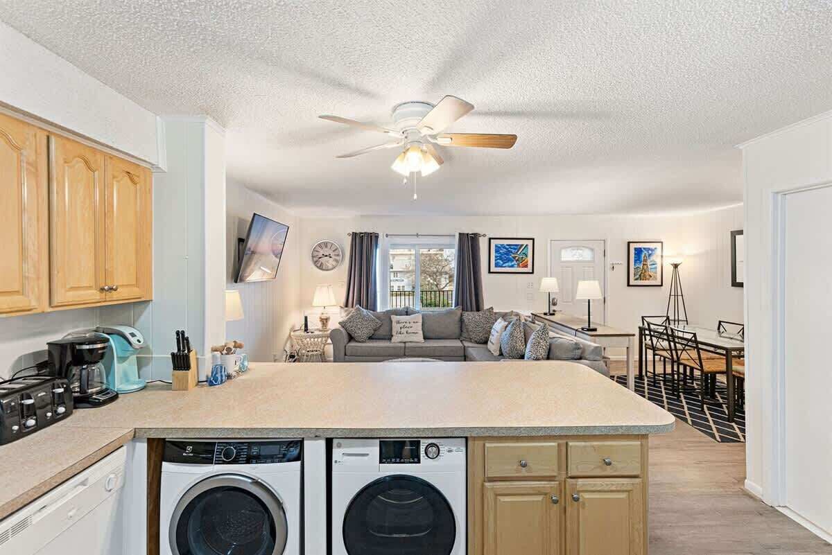 Une cuisine compacte dotée d’un îlot central, d’un lave-linge, d’un ventilateur de plafond et d’un coin repas avec une table et des chaises.