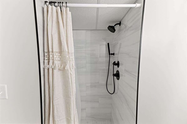 A shower with a white curtain, a handheld showerhead, and a wall-mounted faucet.