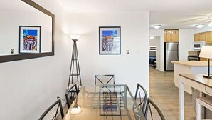 A modern kitchen with stainless steel appliances, a dining area with a glass table, and artwork on the walls.