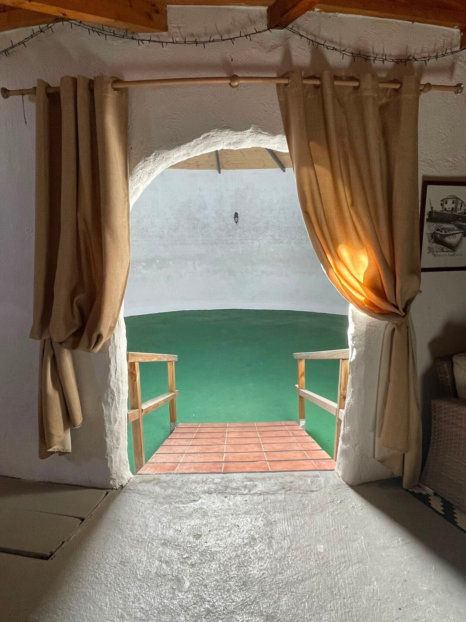 Habitació amb vistes a través d'una finestra amb cortines, una panxa de fusta i una paret verda.