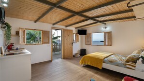 Une pièce avec un plafond en bois, un lit recouvert d’une couverture jaune, un téléviseur fixé au mur et une fenêtre donnant sur un paysage.