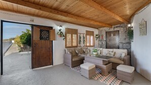 Un espace extérieur abrité, aménagé avec des meubles en osier, un mur en pierre et un plafond en bois.