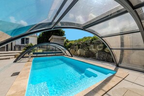 Piscina com vedação de vidro, paredes de pedra e céu azul.