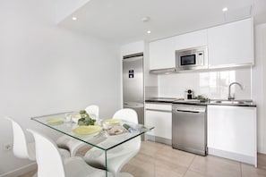 Une cuisine moderne avec des meubles blancs, une table en verre et un lave-vaisselle en acier inoxydable.