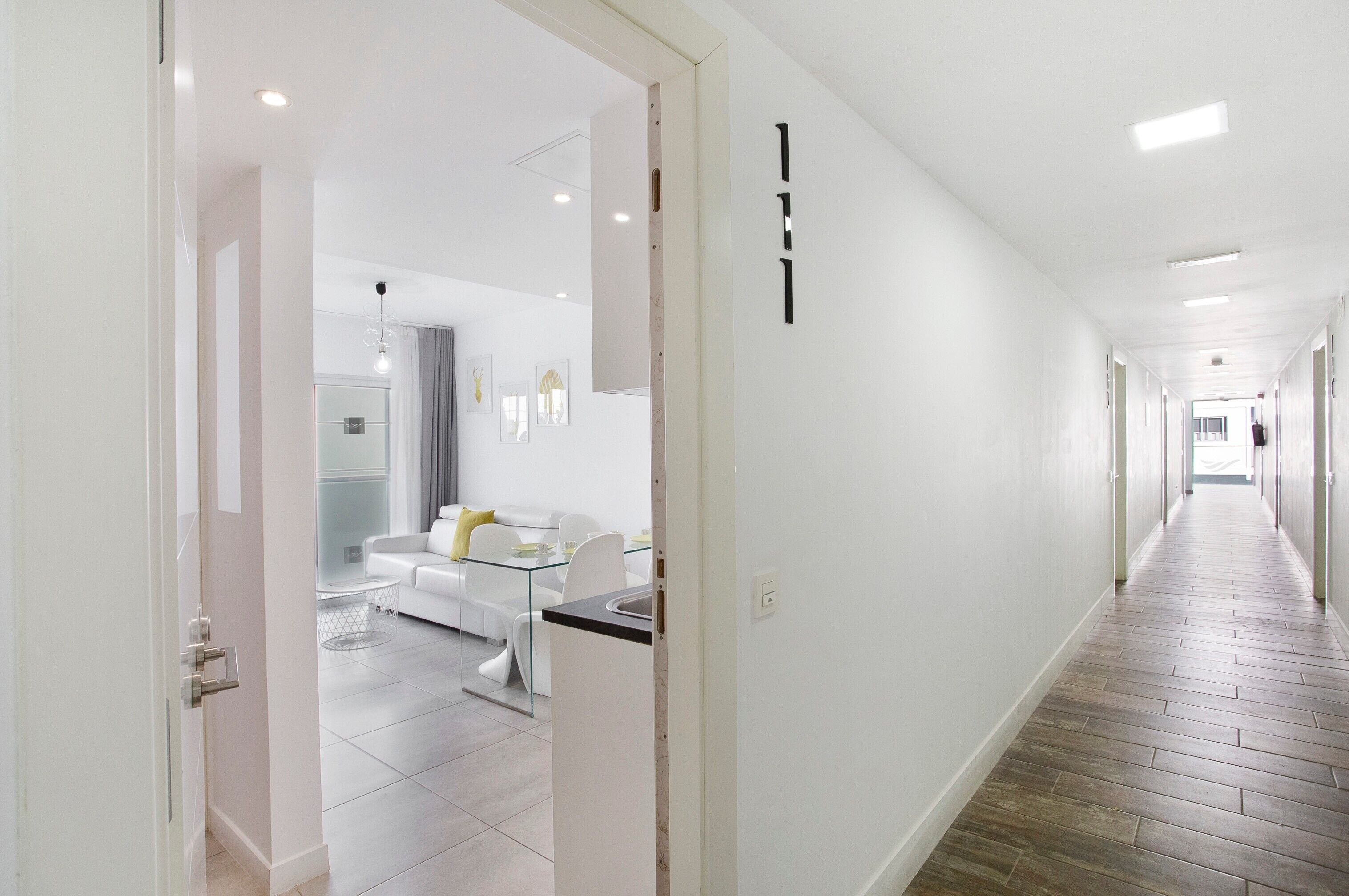 A hallway with a glass table, white sofa, and a door leading to a room.