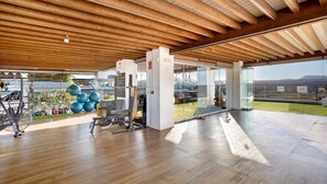 Un gimnasio espacioso con vigas de madera, equipo de ejercicio y grandes ventanales con vistas al exterior.