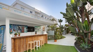 Un bar junto a la playa con mostrador de madera, taburetes y plantas en macetas.
