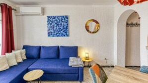 Un sofá azul con una pequeña mesa redonda y una lámpara, una cortina roja y un aire acondicionado instalado en la pared.