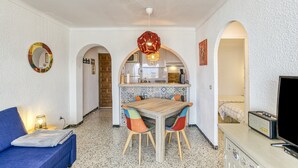 Un espacio habitable compacto con kitchenette, comedor y zona de estar con sofá y televisor.