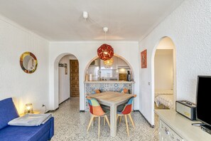 A compact living space with a kitchenette, a dining area, and a seating area with a sofa and a TV.