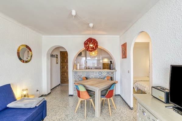 A compact living space with a kitchenette, a dining area, and a seating area with a sofa and a TV.