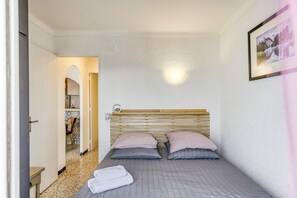 A bedroom with a bed, pillows, a bedside table, a wall-mounted light, and a door leading to a bathroom.